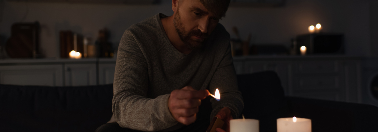 Man lighting candles in a dark South African home during load shedding with several candles already lit on the table in front of him