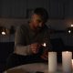 Man lighting candles in a dark South African home during load shedding with several candles already lit on the table in front of him