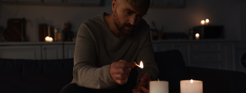 Man lighting candles in a dark South African home during load shedding with several candles already lit on the table in front of him