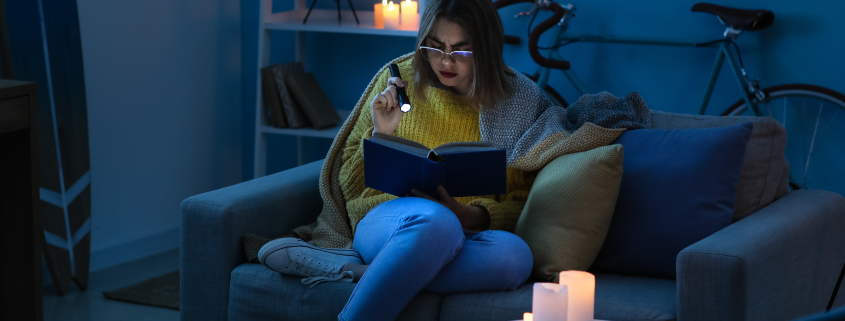 Woman sitting on a couch using a torch to read in a dark home during load shedding in South Africa, highlighting the need for a reliable inverter setup